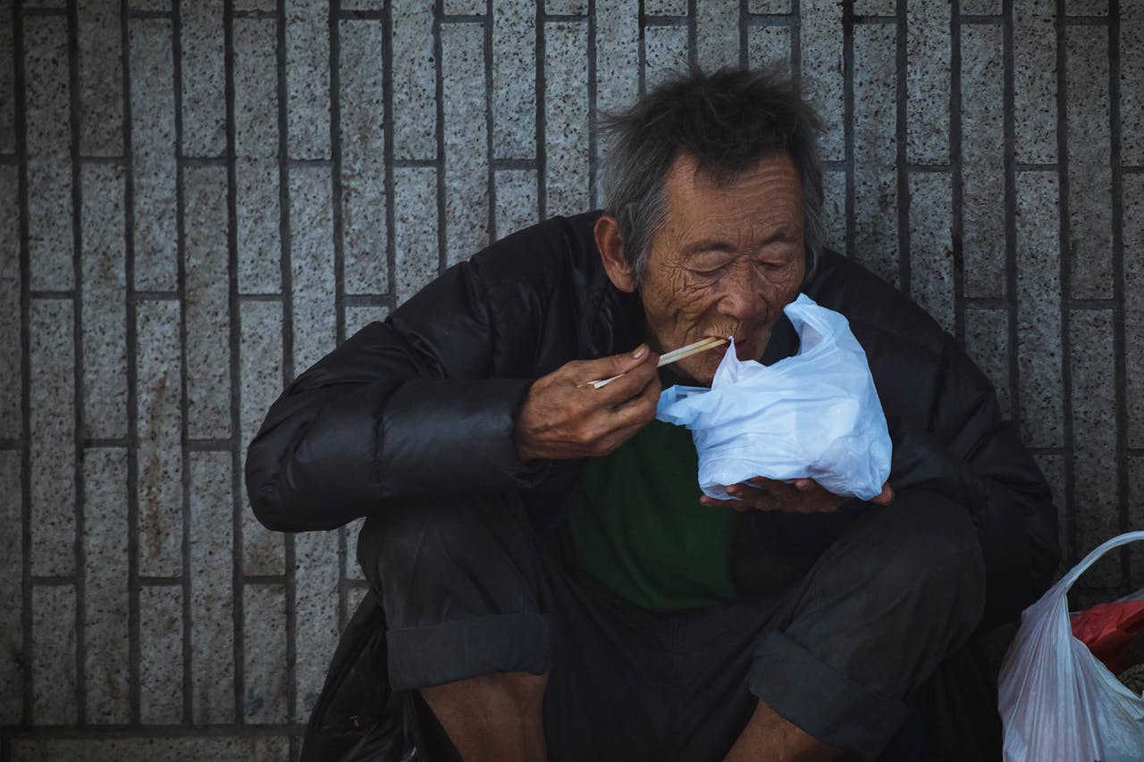 Elderly man sitting and eating on a Kowloon street, capturing urban life.