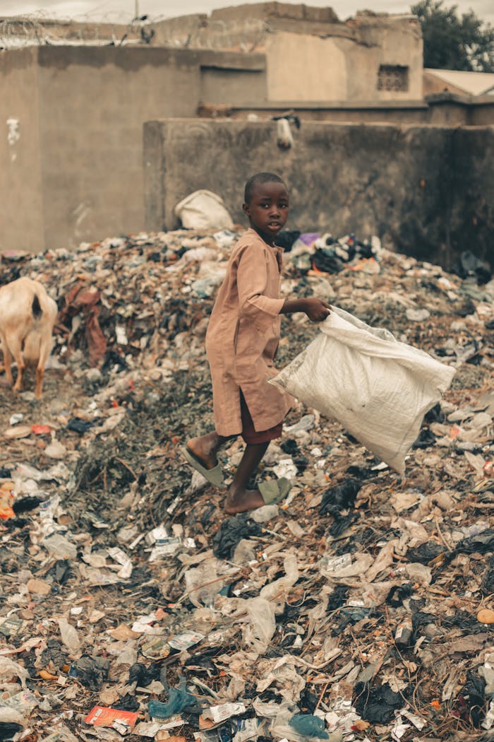Young boy in an urban area collecting recyclables amidst trash piles, highlighting environmental challenges.