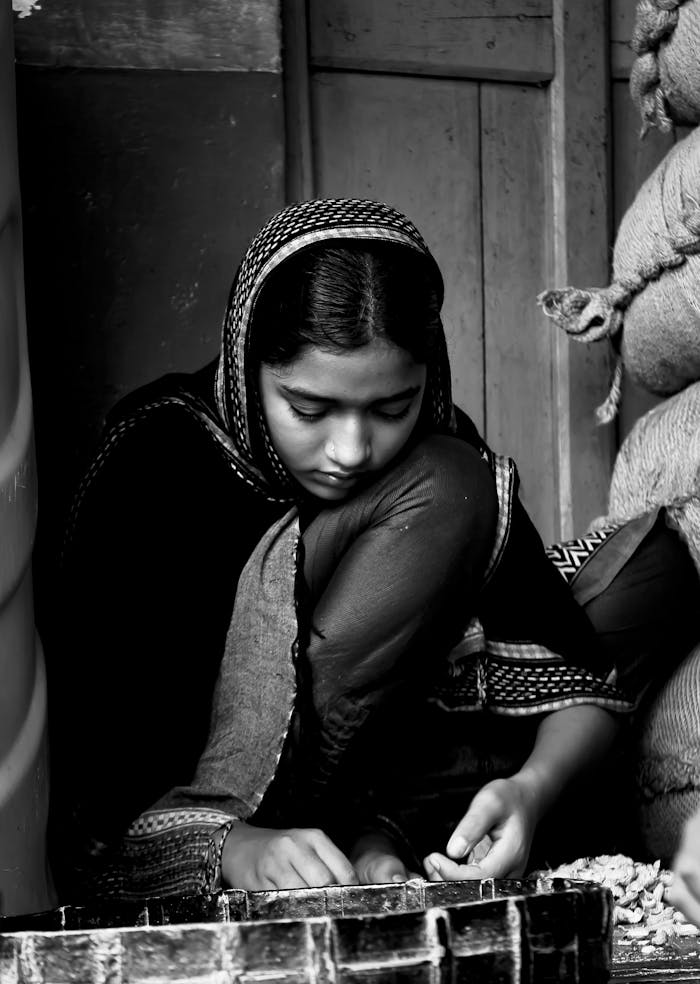 A young girl in a headscarf sorting goods in a traditional market. Black and white image.