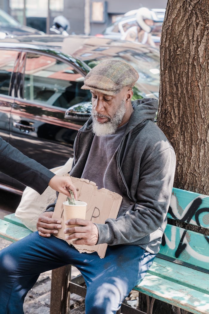 An elderly man seated on a bench receives money in an urban setting.